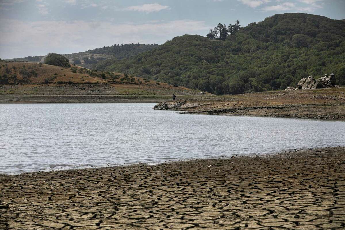 A man fishes at the shoreline of Nicasio Reservoir in Marin County. Next week could bring near-record rainfall to the Bay Area, but the prognosis for the coming rainy season is that it will be drier than average — for the second year in a row.
