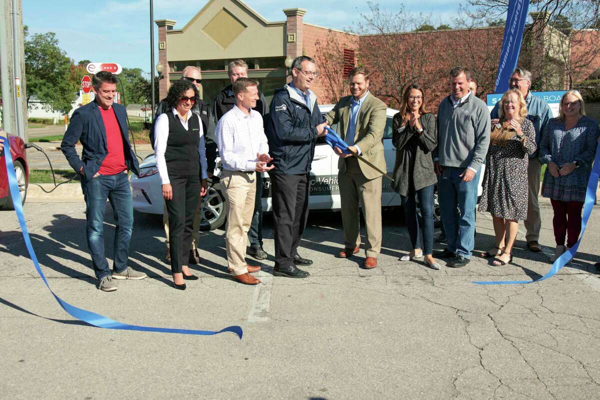 Manistee city manager, William Gambill (center) and to his left, Jeff Myrom of Consumers Energy cut the ribbon on the electric vehicle charging stations in the Washington Street parking lot. (Jeff Zide/News Advocate)