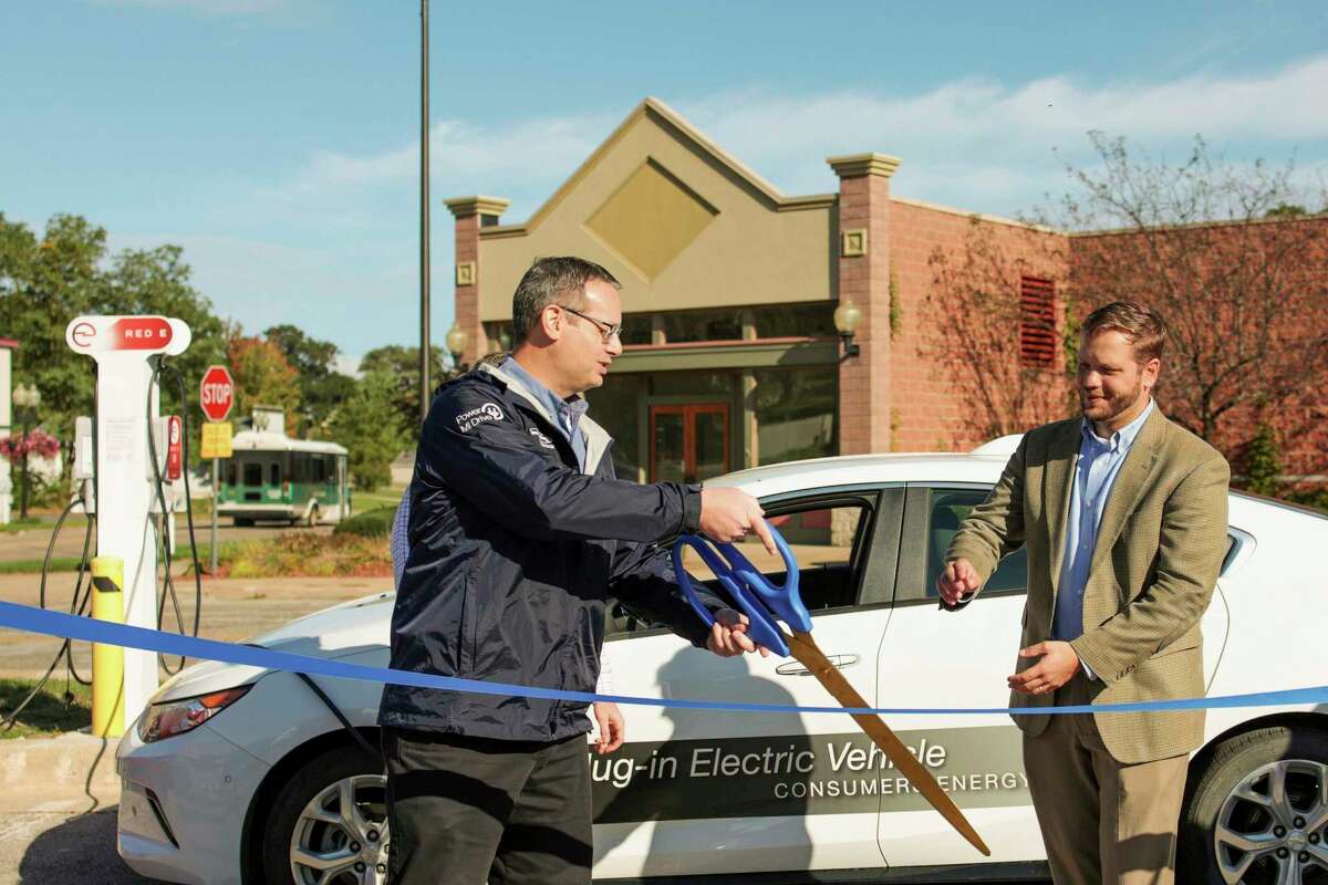 Jeff Myrom of Consumers Energy presents a giant scissors to Manistee City Manager William Gambill during a ribbon-cutting ceremony for electric vehicle charging stations in Manistee. (Jeff Zide/News Advocate)