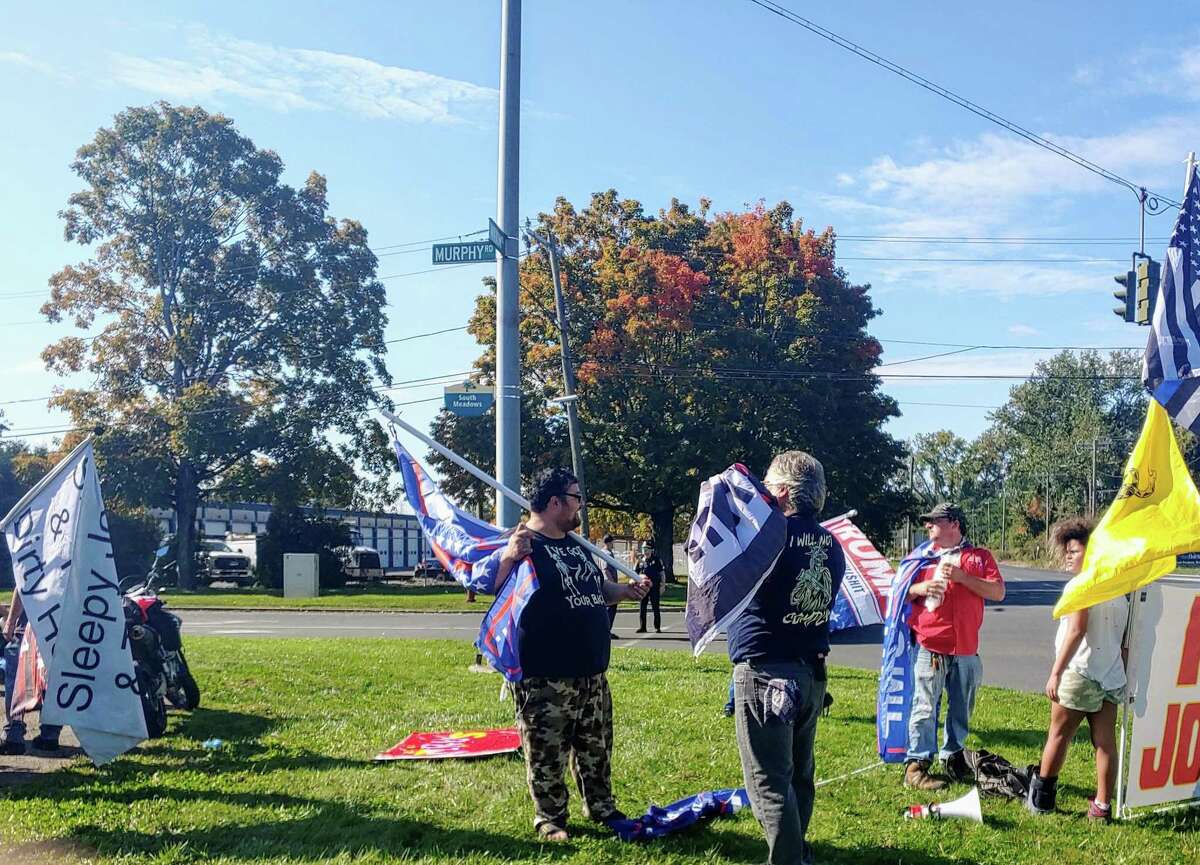 Members of “Debbie’s Deplorables” brandish signs and banners to greet and critisize President Joe Biden when he lands at the Brainard Airport in Hartford Oct. 15, 2021.
