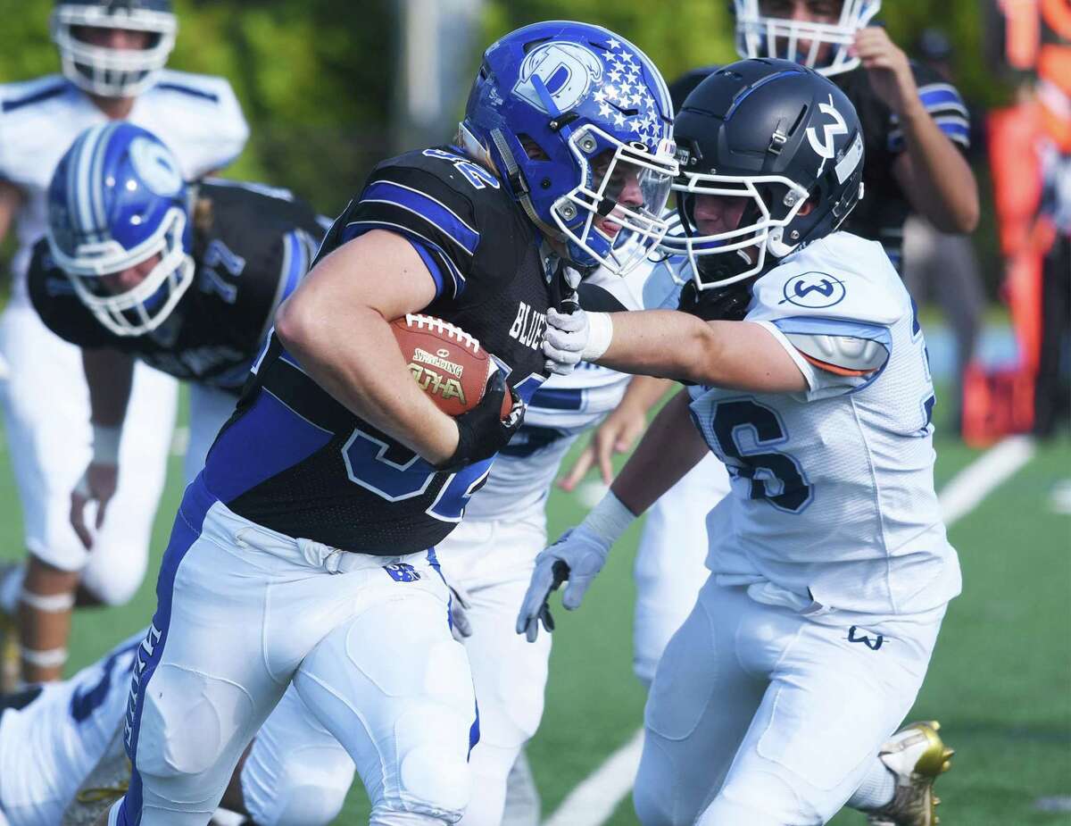 Darien's Tighe Cummiskey (32) pounds out some rushing yards while Wilton's Todd Woodring (36) attempts to slow him down during a football game in Darien on Saturday, Oct. 16, 2021.