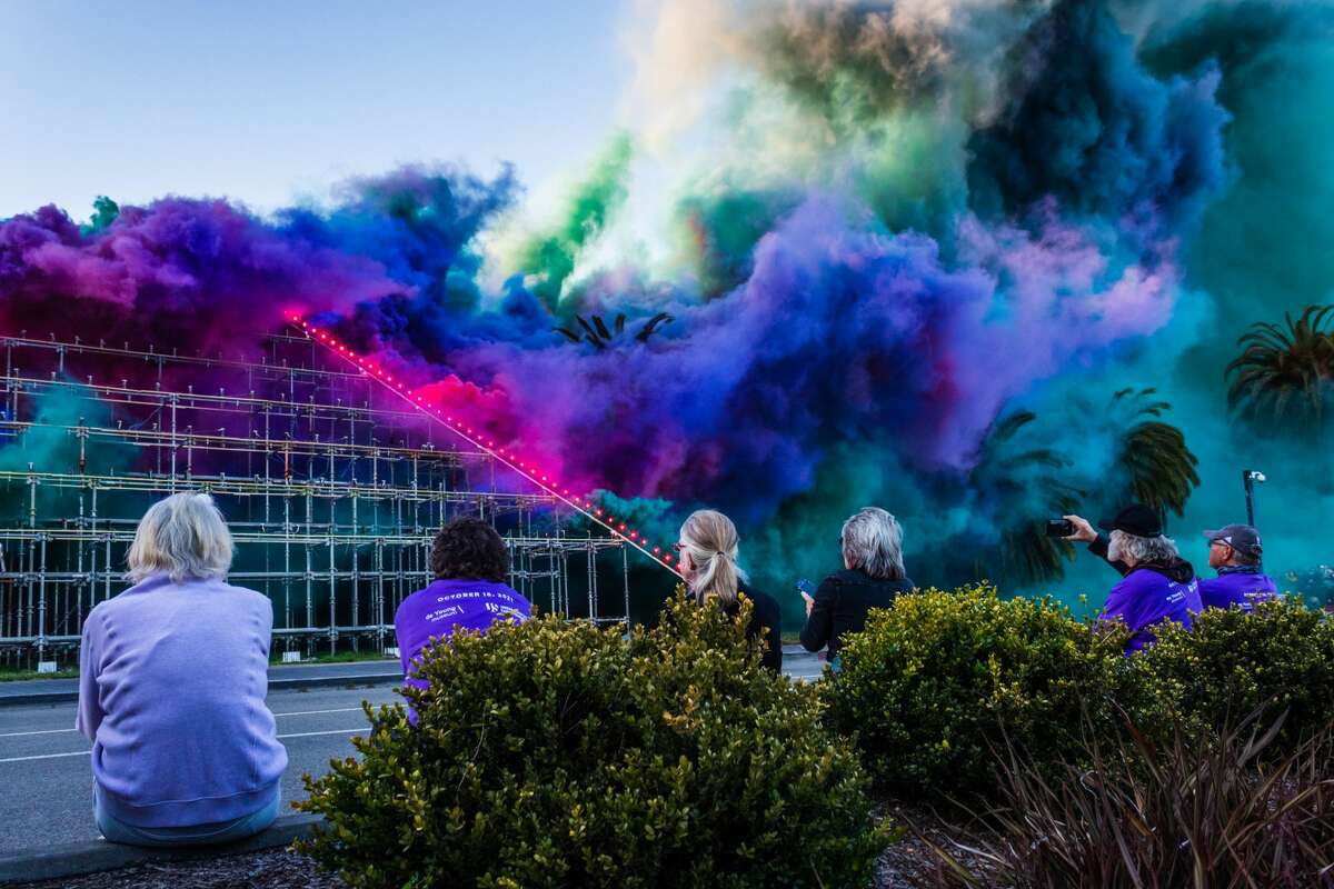 Colorful smoke plumes rise and drift east through San Francisco during Judy Chicago's Forever de Young installation watched by event staff and volunteers on October 16, 2021 (Kevin Kelleher / Special for SFGATE)