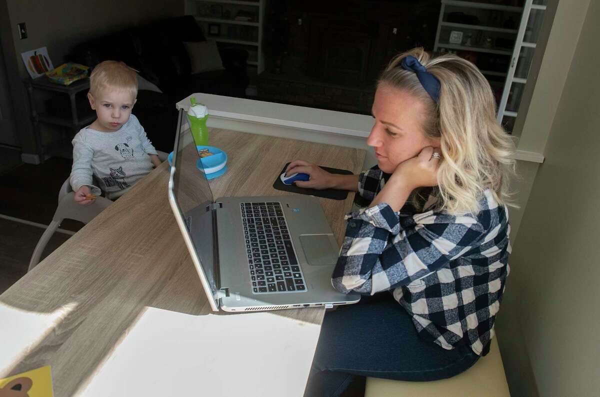 Emily Kusaywa works while her toddler Tanner eats a snack on Wednesday, Oct, 20, 2021 in Ballston Spa, N.Y. Kusaywa, who works from home, is one of many parents in the Capital Region looking for affordable child care.