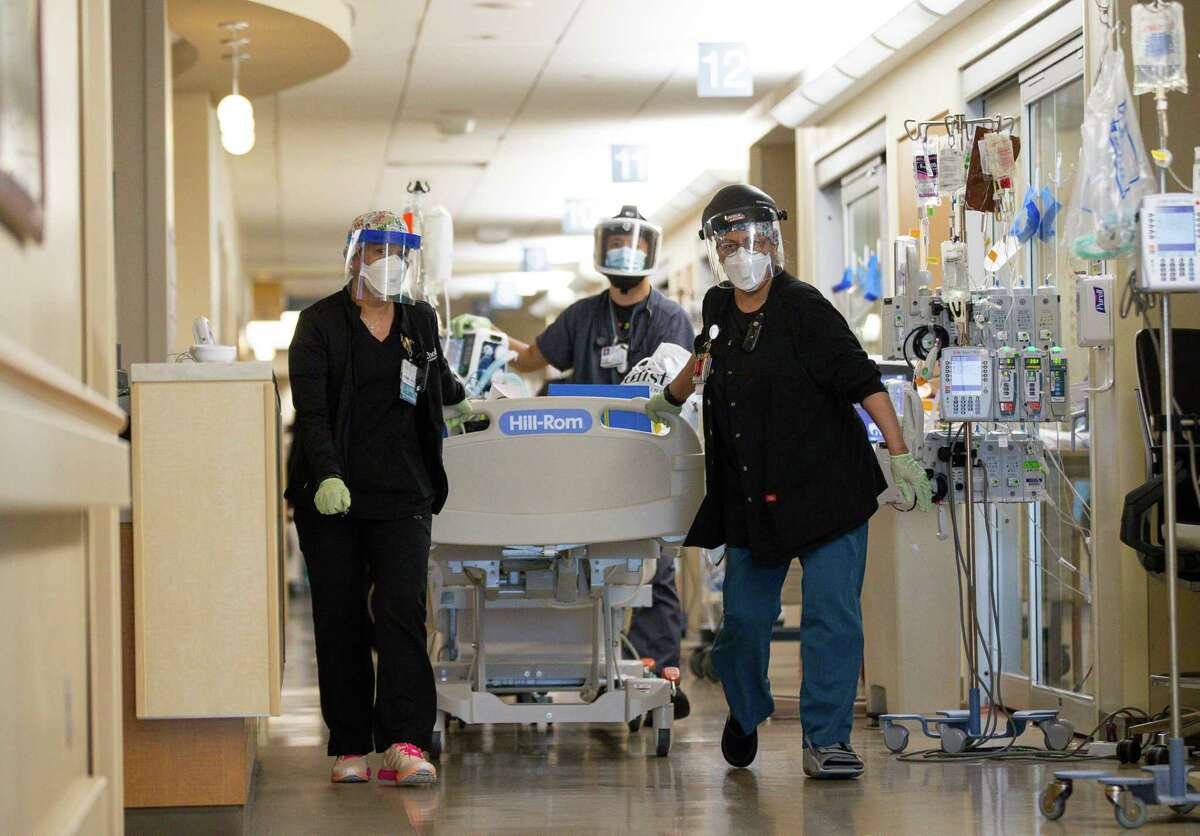 Medical professionals usher a patient who was being transported into a Houston Methodist Hospital ICU room on Thursday, Sept. 2, 2021, in Houston. The room to which the patient was being moved into had just become available after another patient was downgraded from the unit. The long queue of patients needing ICU care means beds are filled rapidly.