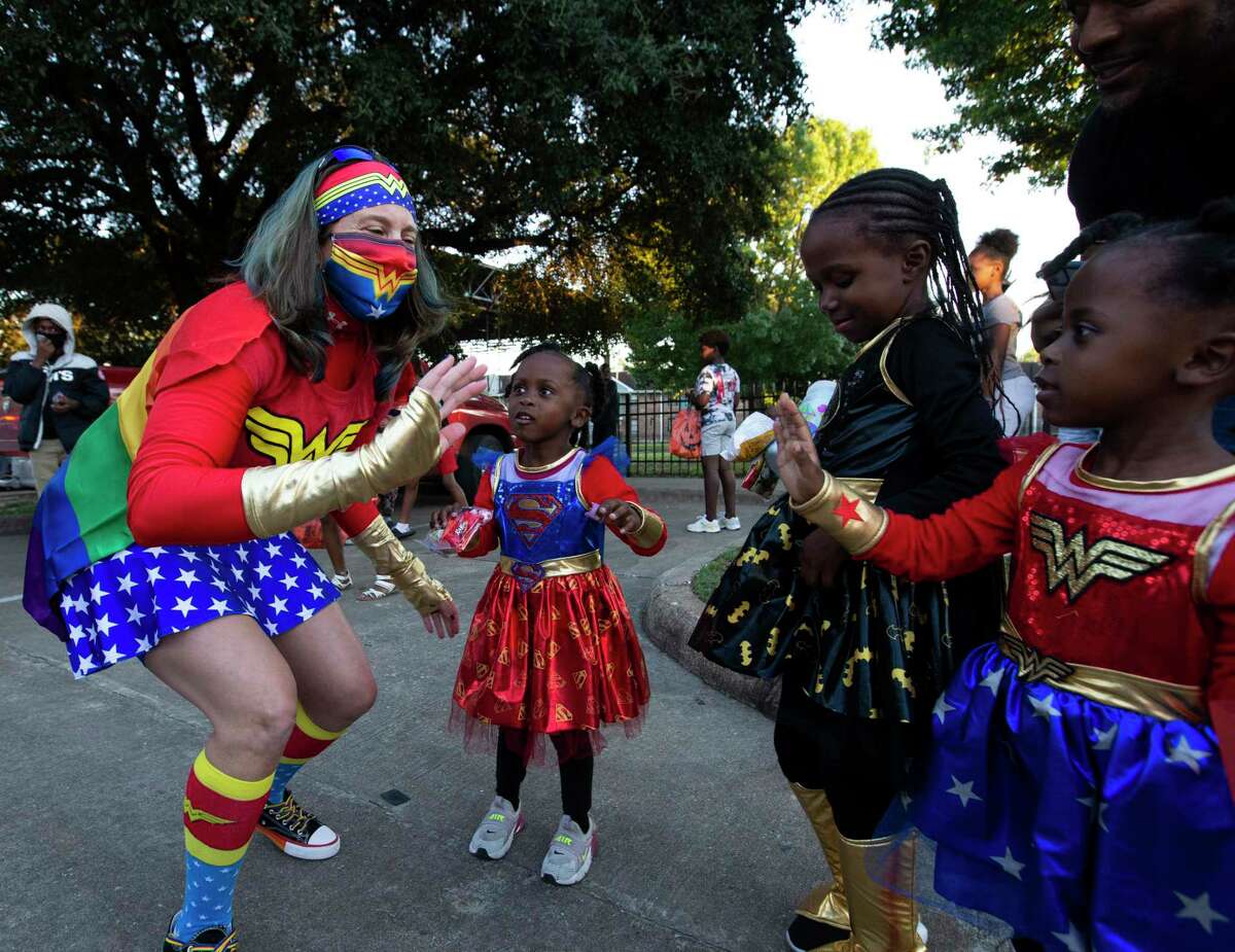 Wonder Woman Kristy Miller meets mini Wonder Woman twins Tori and Tira Frazier, 4, and their Batwoman sister, Tali Frazier, 6, as Houston Police Department South Central Patrol are bringing Halloween to neighborhoods and handing out candies with the “Rollin Trunk or Treat” caravan Friday, Oct. 30, 2020, at Cuney Homes in Houston.