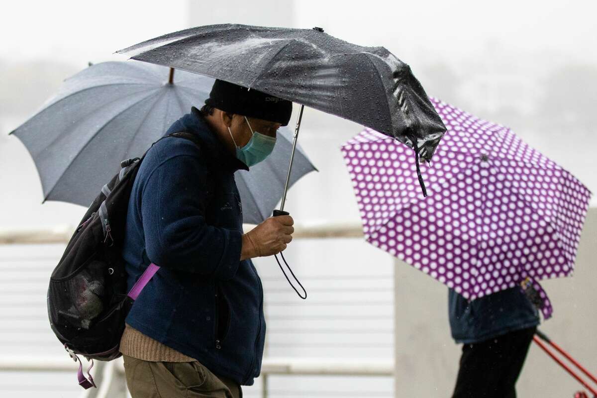 Pedestrians use umbrellas during a rain shower near Lake Merritt in Oakland, California on Oct. 21, 2021.