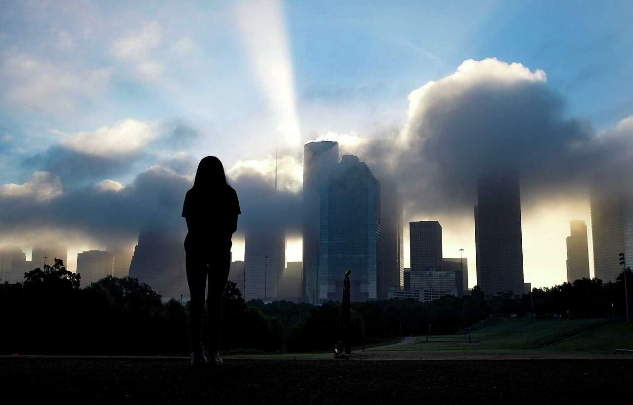 A woman watches an early morning fog rolls out of downtown Houston from Eleanor Tinsley Park on Thursday, Oct. 21, 2021