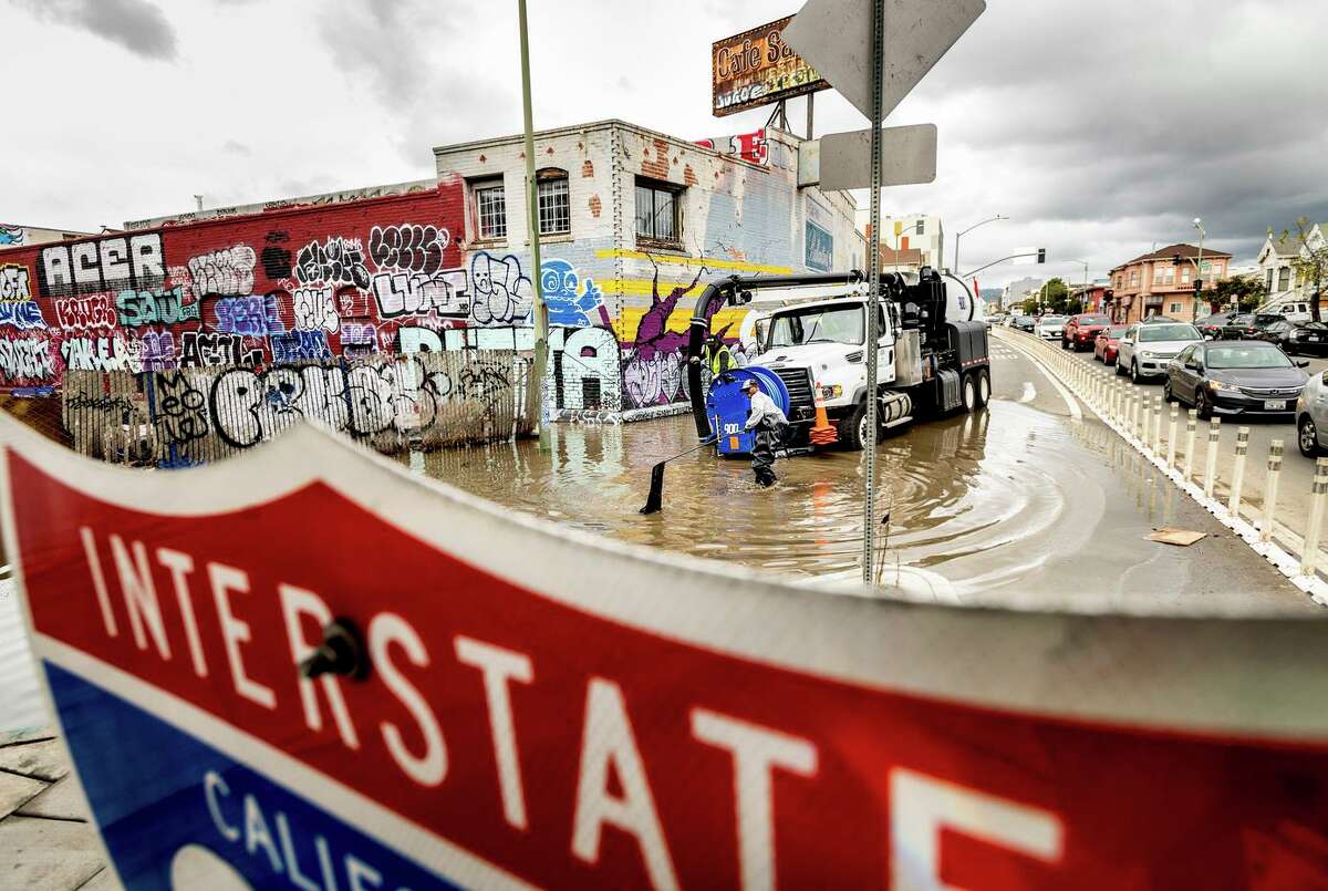 Barry Nixon works to clear a clogged drain at Jackson and 6th streets in Oakland on Friday. The flooding, adjacent to a homeless camp, closed an entrance to Interstate 880.