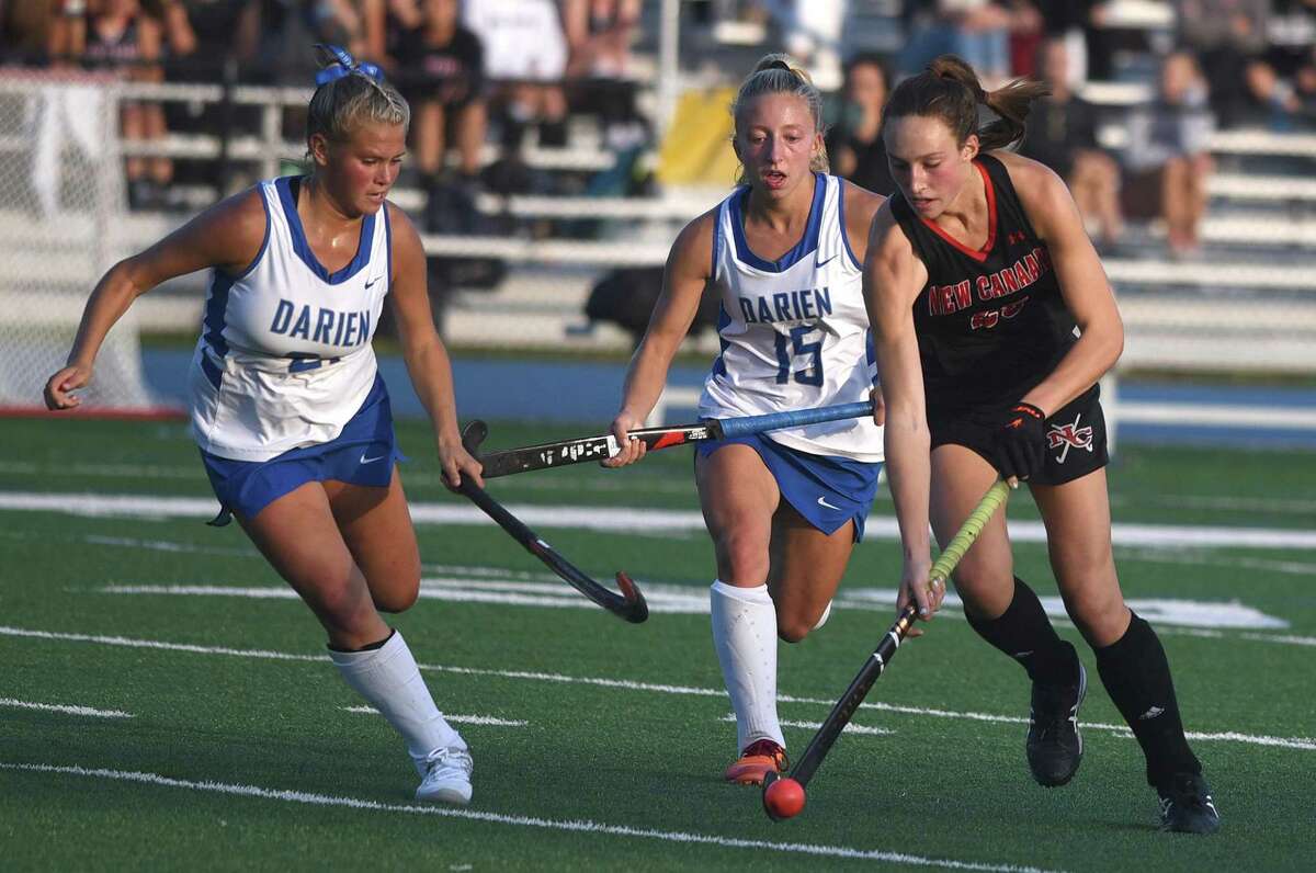 New Canaan's Polly Parsons-Hills (25) brings the ball through the midfield while Darien's Molly McGuckin (21) and Kaci Benoit (15) defend during a field hockey game in Darien on Friday, Oct. 22, 2021.