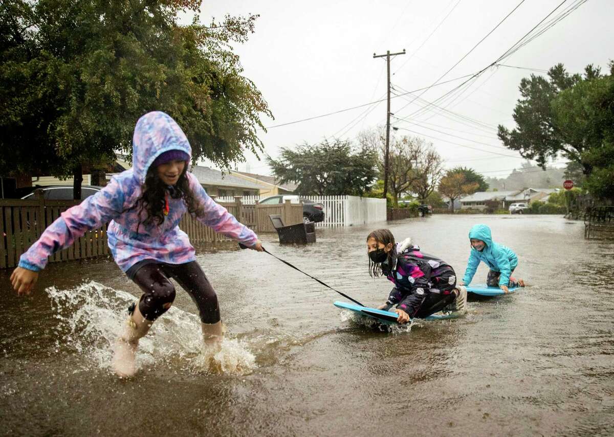 Children play in floodwaters on Robin Road in Mill Valley as the atmospheric river storm sweeps the Bay Area and Northern California beyond.