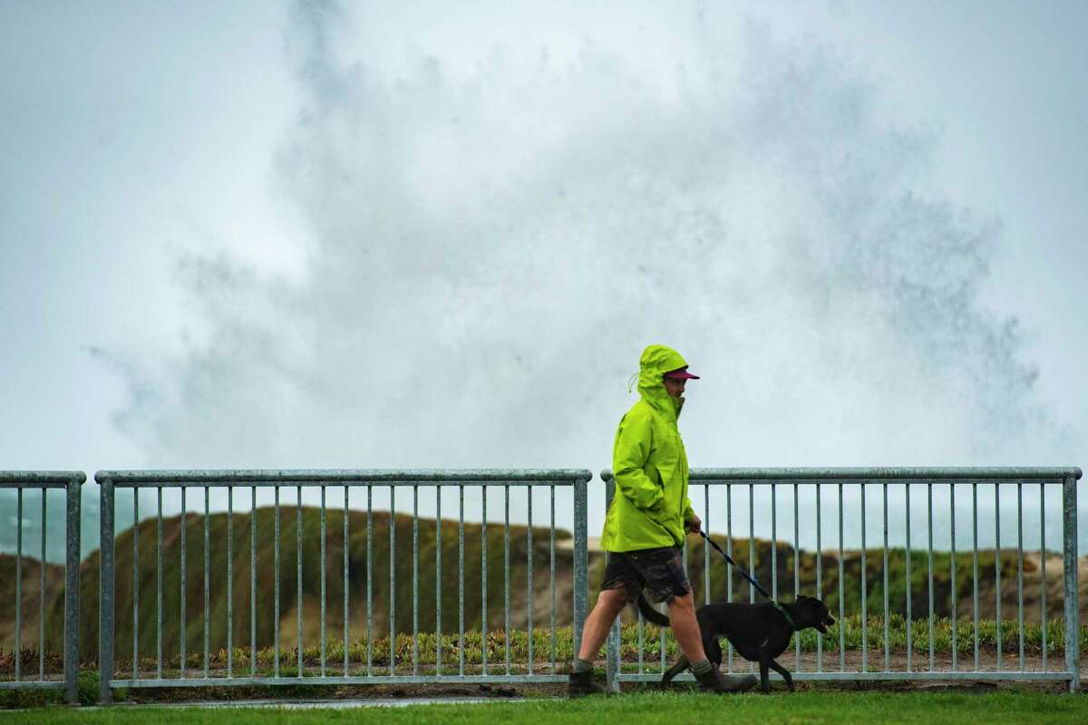 A man walks his dog along Lighthouse Point as large waves brought in by a storm surge crash in Santa Cruz on Sunday.