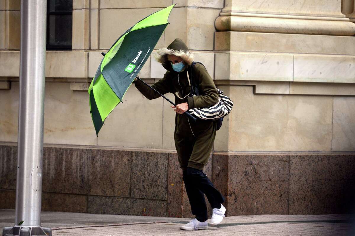 A woman holds onto her umbrella against a strong wind while walking along Main Street in downtown Bridgeport, Conn.