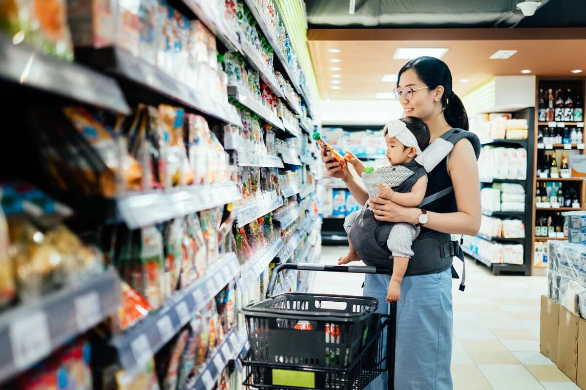Smiling young mother grocery shopping with baby girl in supermarket. 
