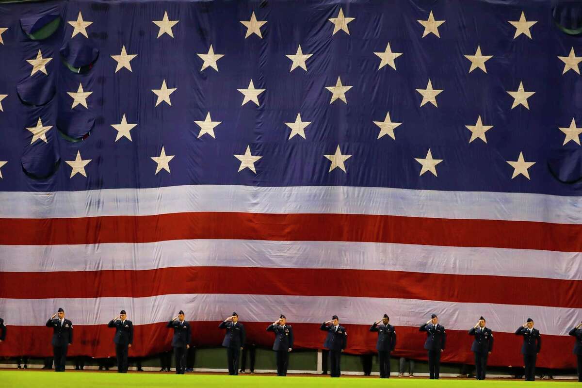 An American Flag is draped over the Green Monster in left field during the National Anthem before Game 3 of the American League Championship Series on Monday, Oct. 18, 2021, at Fenway Park in Boston.