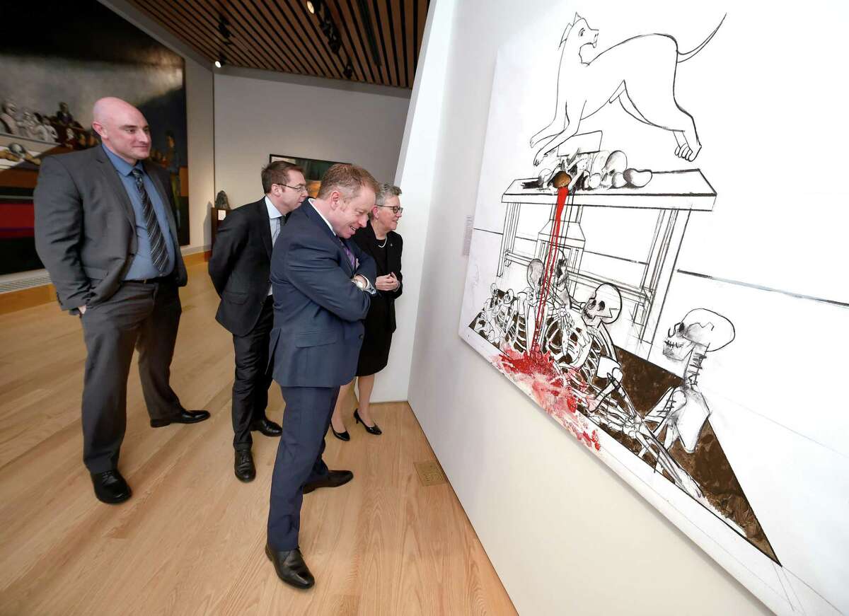 Ciaran Cannon (center), Irish Minister of State at the Department of Foreign Affairs and Trade, views The Wounded Wonder by Michael Farrell during a visit to Quinnipiac University's Great Hunger Museum in Hamden on February 8, 2018.