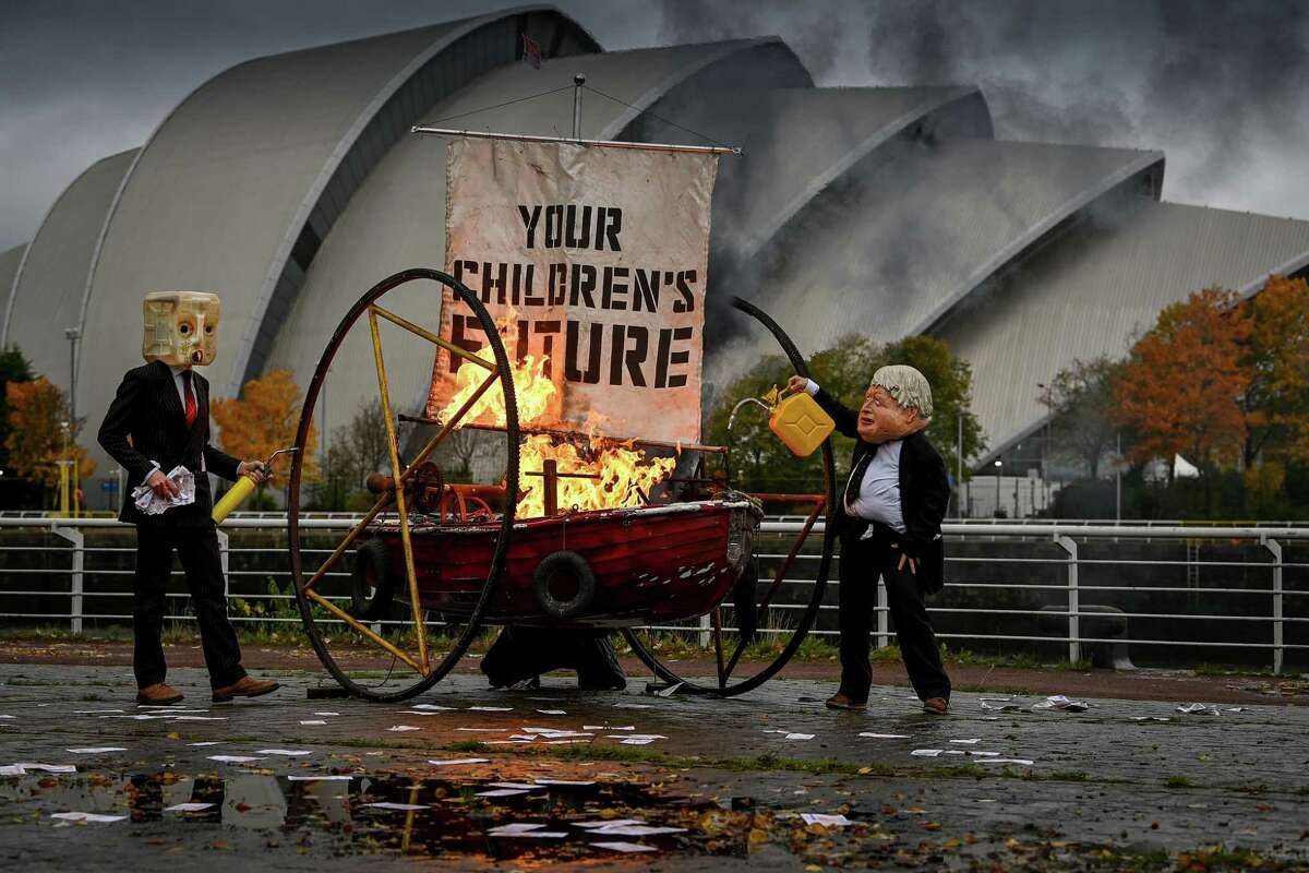 Activists from Ocean Rebellion dressed as Boris Johnson and an Oilhead set light to the sail of a small boat as they protest next to the River Clyde opposite the COP26 site on October 27, 2021 in Glasgow, Scotland. The Extinction Rebellion-affiliated group staged their protest on the banks of the River Clyde, opposite the Hydro building, one of the venues of the coming COP26.