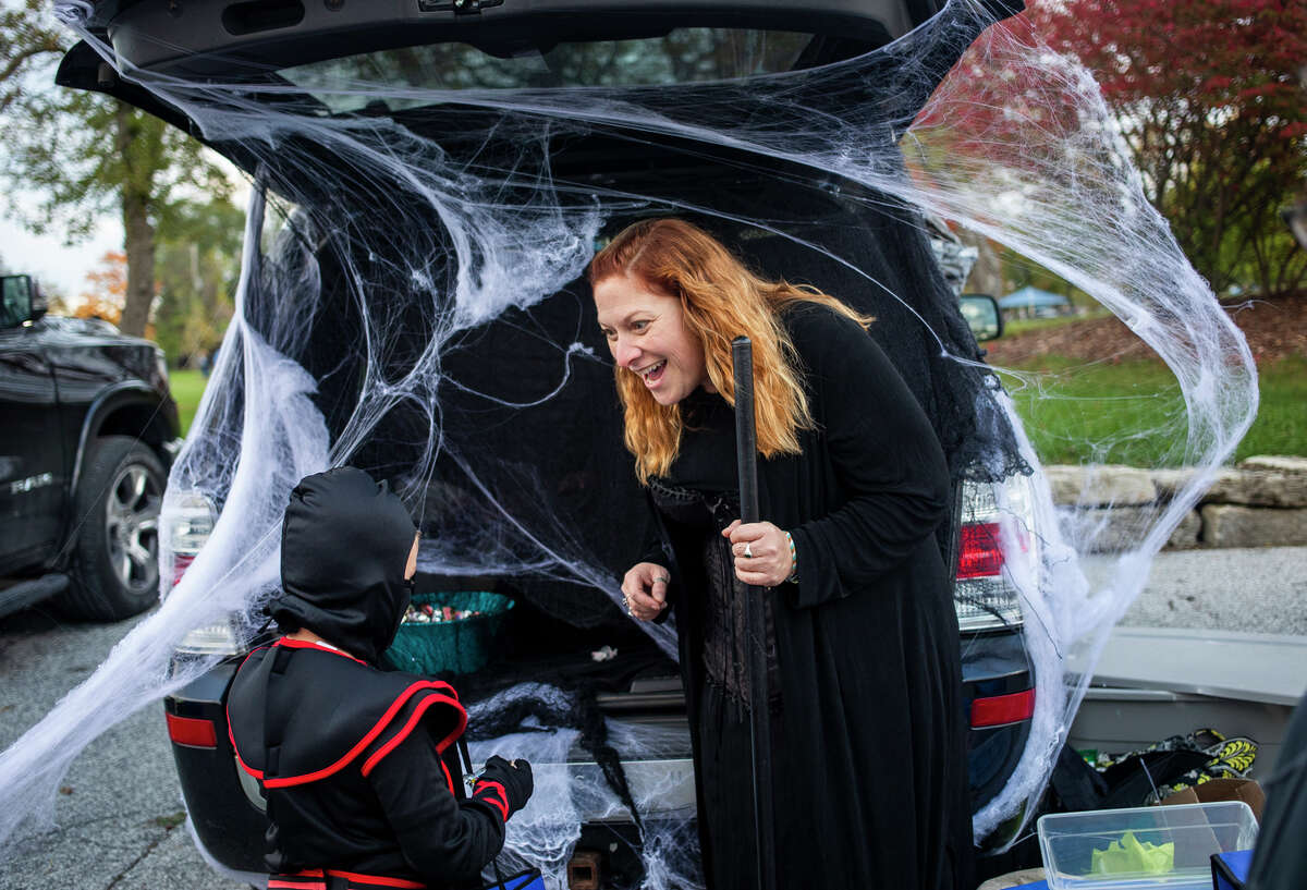 Stephanie Curtis, dressed as a witch, right, greets Bryson Pesta, dressed as a ninja, 5, left, while passing out candy during a trunk-or-treat event Thursday, Oct. 28, 2021 at Grove Park in Midland. (Katy Kildee/kkildee@mdn.net)
