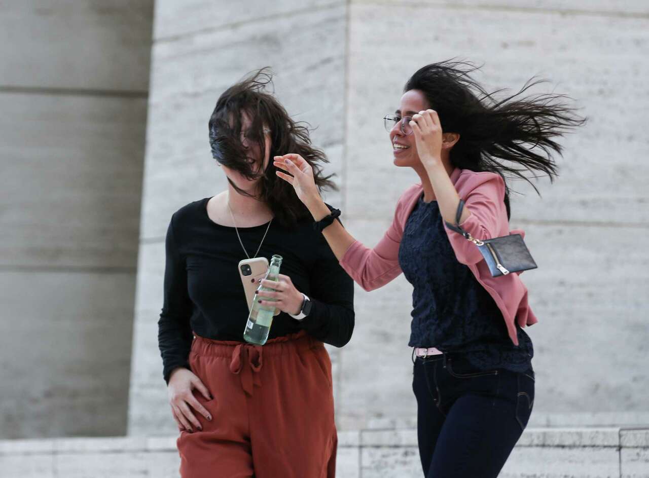 Two women struggle with their hair in high winds Thursday, Oct. 28, 2021, in downtown Houston.