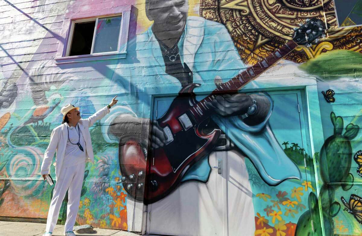Grammy Award-winning musician Carlos Santana shows the part of the mural where his brother Jorge Santana is depicted during the dedication and blessing ceremony in honor of their family.