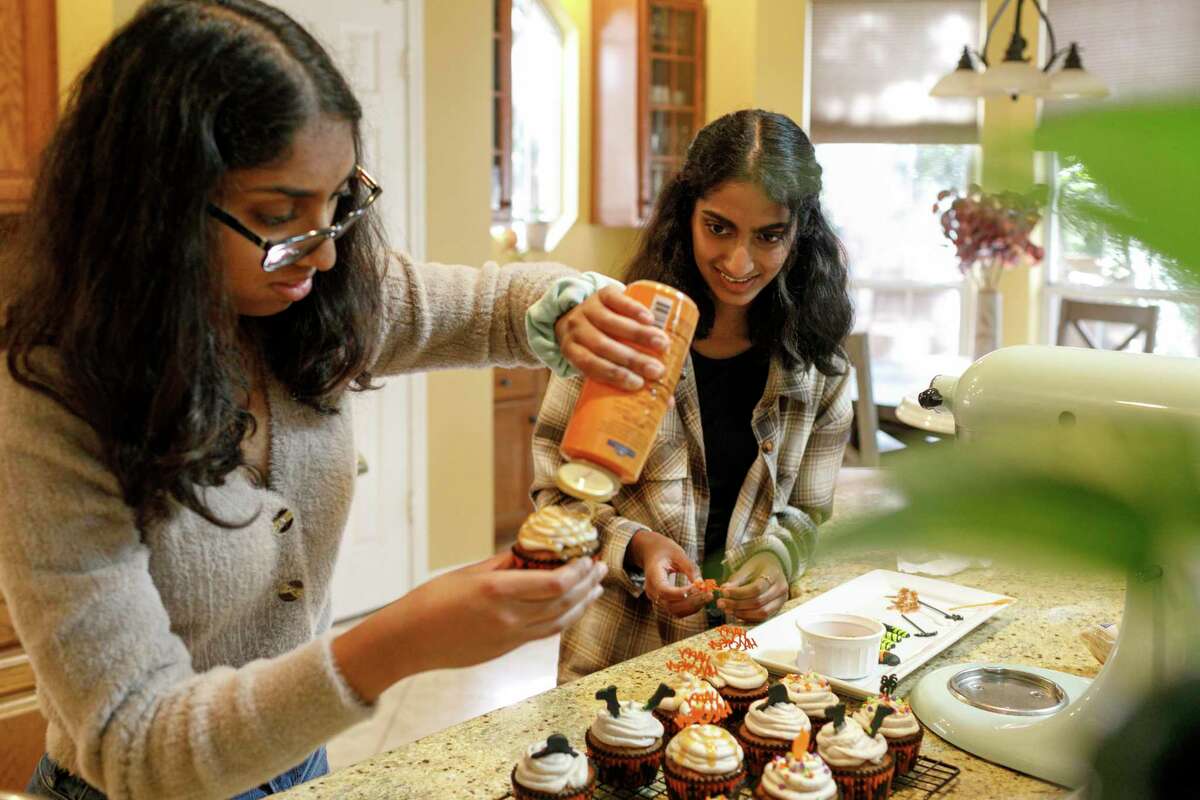 Thirteen-year-old Hena Abdul, right, watches her 16-year-old sister, Eliza, left, drizzle caramel sauce on one of their freshly made pumpkin spice cupcakes in their San Antonio home kitchen Saturday, Oct. 23. The sisters work together to plan out menus and sell baked goods from their online bakery business called “Whisk’N Cake.”