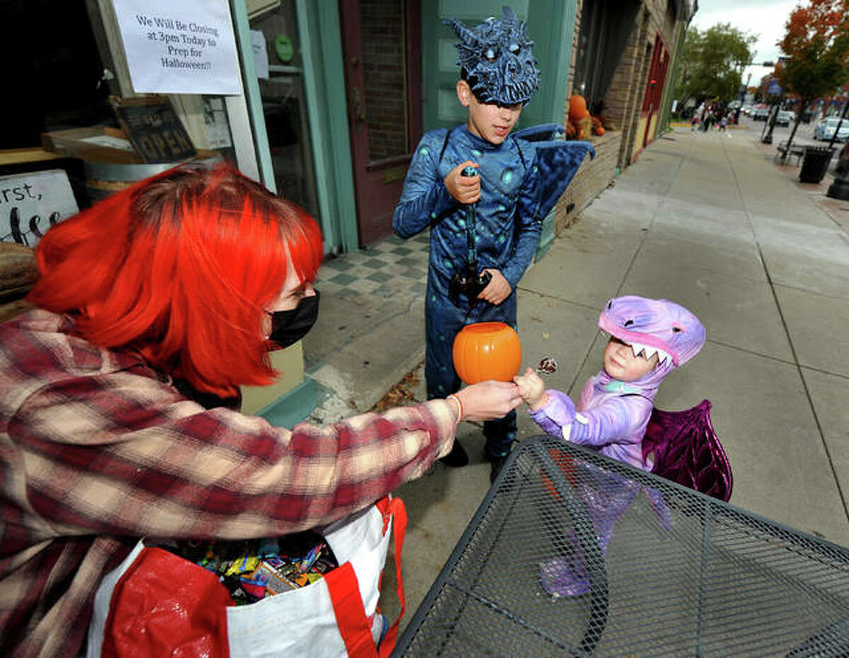 Ellie Tschida, 2, of Edwardsville, right, takes a lollipop from Sarah Harmon, left, in front of 222 Artisan Bakery as she and her brother Joshua, 9, attend the Halloween Trick-or-Treating in downtown Edwardsville Saturday.