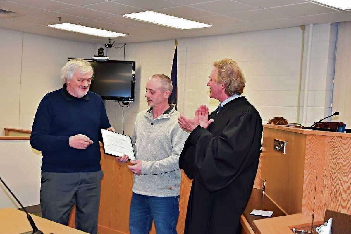 Manistee County District Judge Thomas Brunner (right) and Daryl Goodman (left), sobriety court case manager, handed Chris Gee (center) his certificate of achievement and a card after telling the courtroom full of sobriety court team members, participants and supporters how much of a pleasure it had been to work with Gee in the program. Gee was the program's first graduate and he finished the program in February 2020. 
