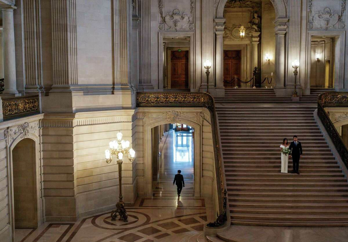 A couple poses for wedding photos on the steps of the rotunda as City Hall welcomes employees back to San Francisco after more than a year and a half of remote work.