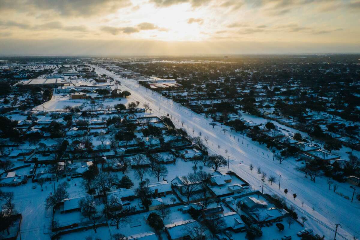 Aerial view of Dallas homes and roads covered in a layer of snow with the sunrise in the distance. The 2021 winter storm dropped up to 10 inches of snow and saw temperatures dip as low as zero degrees.