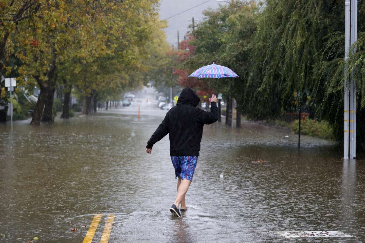 A pedestrian carries an umbrella as he walks on a flooded street on October 24, 2021 in San Rafael.