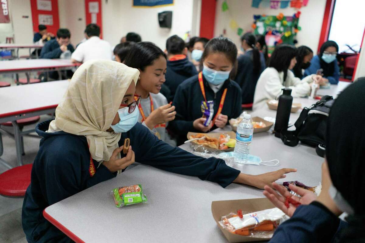 在奥克兰AIMS学校，八年级学生Nawf Abuelgasim(左)在午餐时间与同学们分享零食。学生可以在吃饭时摘下口罩。