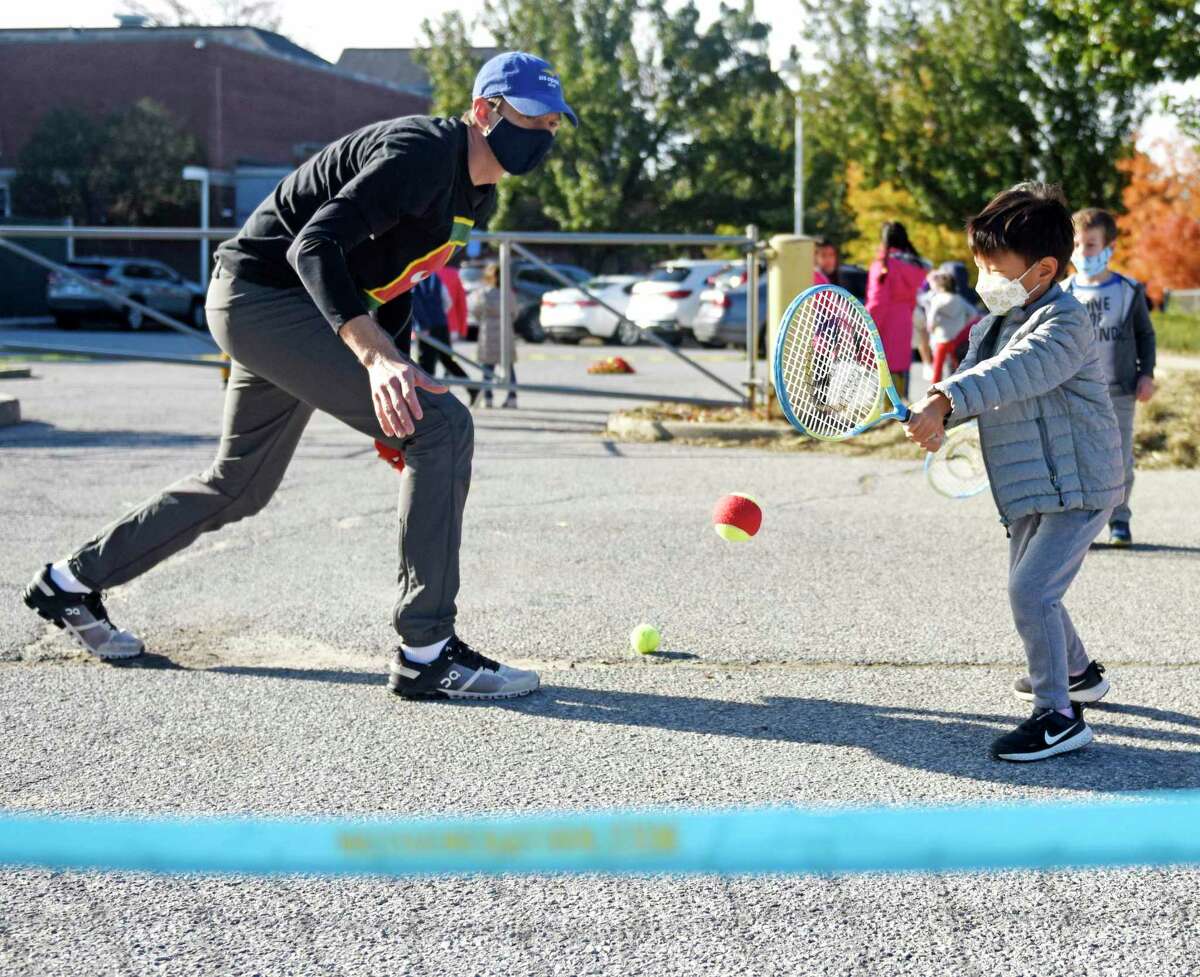 Former tennis pro Eric Butorac tosses a ball to kindergartner Sean Song during a tennis class at Cos Cob School in the Cos Cob section of Greenwich, Conn. Thursday, Nov. 4, 2021. The former tennis doubles specialist lives in Cos Cob and his children attend school in Greenwich, so he took a day to teach tennis to kids during gym class at Cos Cob School. The students learned the basics of tennis and completed drills individually and in small groups.