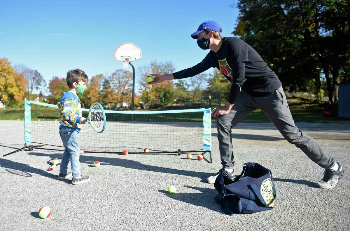 Former tennis pro Eric Butorac tosses a ball to kindergartner Leo Myder during a tennis class at Cos Cob School in the Cos Cob section of Greenwich, Conn. Thursday, Nov. 4, 2021. The former tennis doubles specialist lives in Cos Cob and his children attend school in Greenwich, so he took a day to teach tennis to kids during gym class at Cos Cob School. The students learned the basics of tennis and completed drills individually and in small groups.