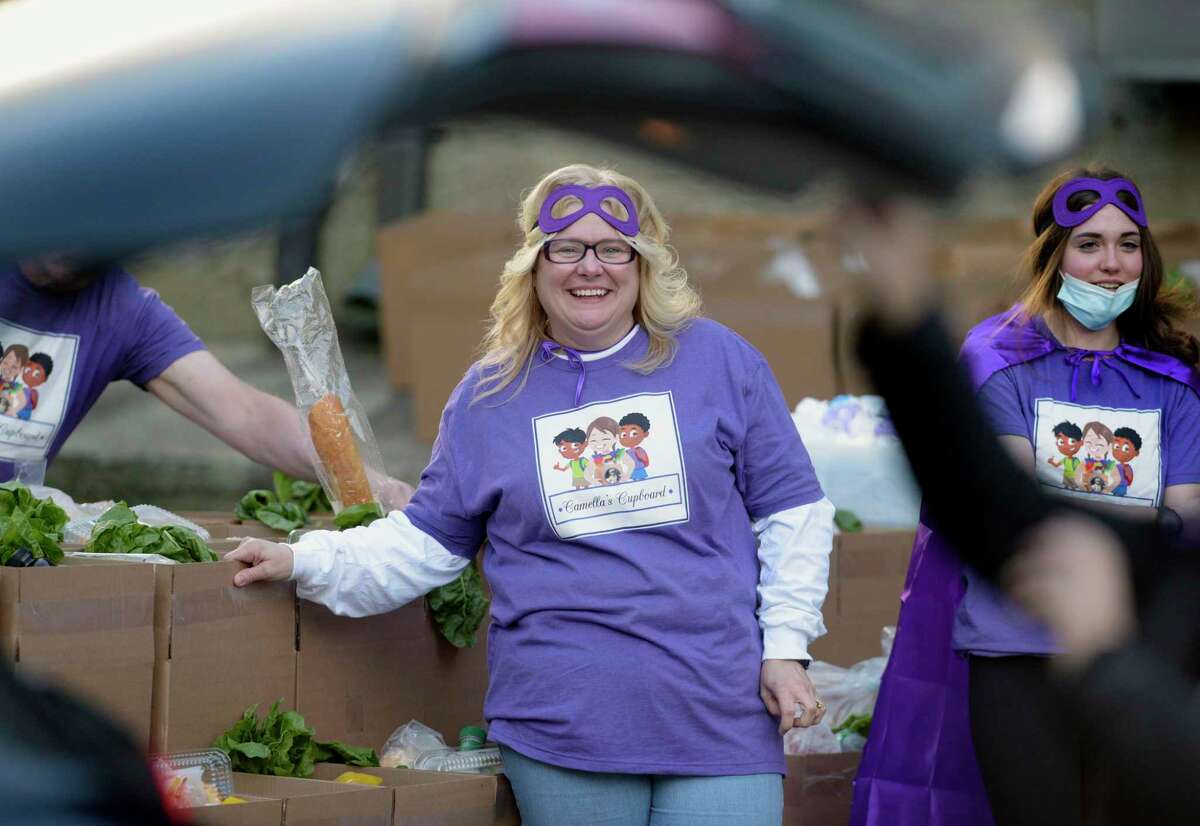 Angie Chastain, founder and executive director of Camella’s Cupboard, watches as volunteers help distribute food on Friday, Oct. 29, in New Milford. Everyone was dressed for Halloween in purple capes and masks.