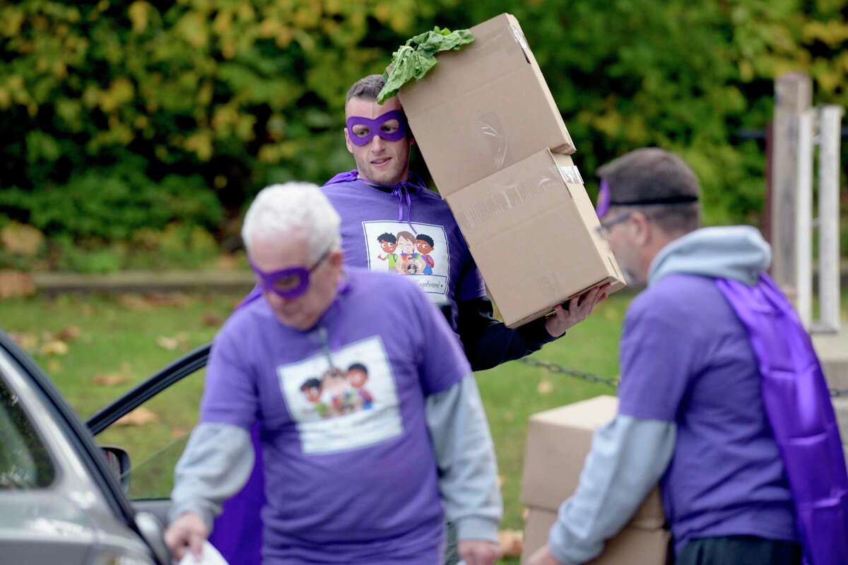 Volunteer Justin Cullmer carries boxes of food to a clients car during the food distribution for Camella’s Cupboard in New Milford on Friday afternoon. Everyone was dressed for Halloween in purple capes and masks.