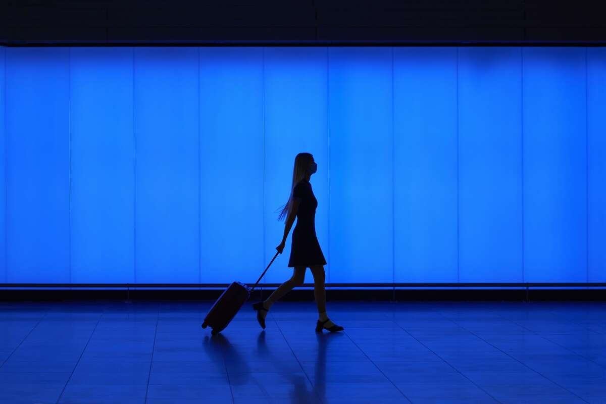 A file image of a silhouette of a woman walking with her trolley luggage against blue light panels. 