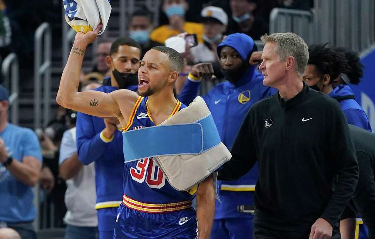 Warriors guard Stephen Curry (left) reacts toward teammates next to head coach Steve Kerr on the bench.