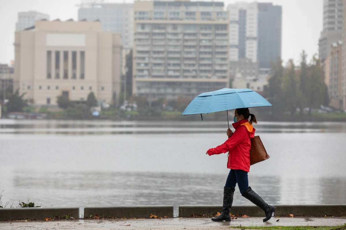 FILE: A woman walks along Lake Merritt during a rainfall in Oakland, Calif. on Nov. 9, 2021.