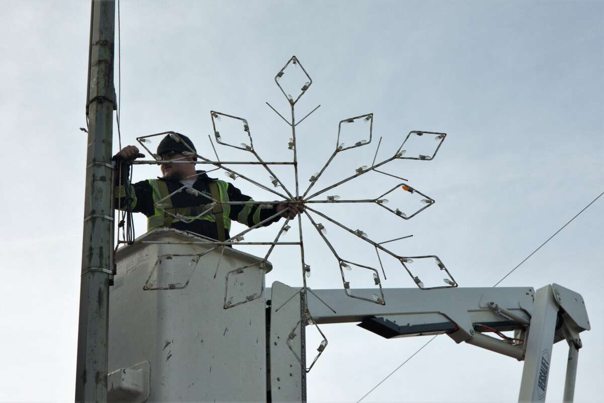 Workers from the Department of Public Works attach giant snowflakes to various power poles on Tuesday in Manistee. Workers hung snowflakes along U.S. 31 from First Street to Filer Street and on Maple and First streets, among other locations. 