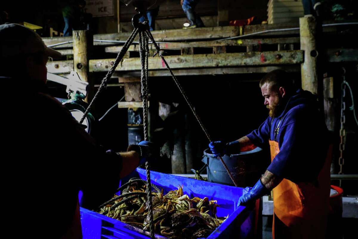 Fisherman Jake Wilson (right) prepares a container of Dungeness crab to be hauled up to shore at Fishermans Wharf in San Francisco in December 2019.