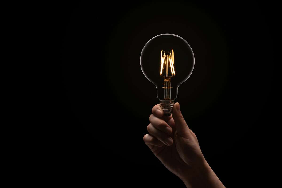 A hand holds an illuminated light bulb in the dark. 