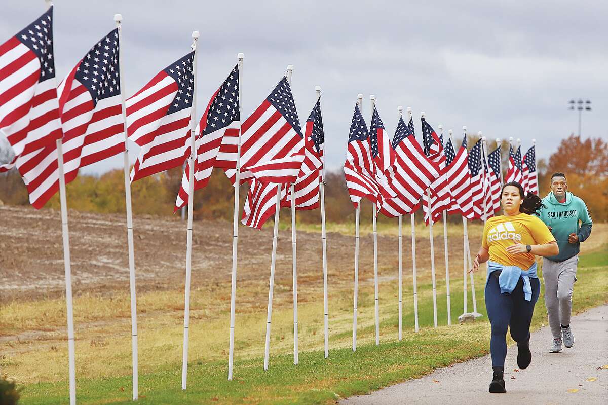 John Badman|The Telegraph Two hearty runners, who didn't seem to mind the morning chill, run past some of the Avenue of Flags set up for Veterans Day Thursday in front of Godfrey's Glazebrook Park.