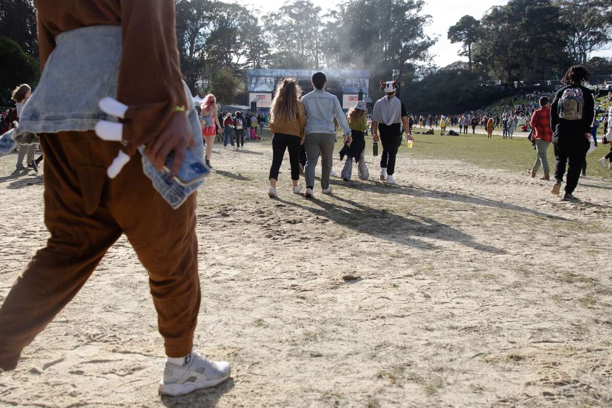 People walk across sand that had been spread out to cover muddy areas of grass at Outside Lands in Golden Gate Park on October 31, 2021.