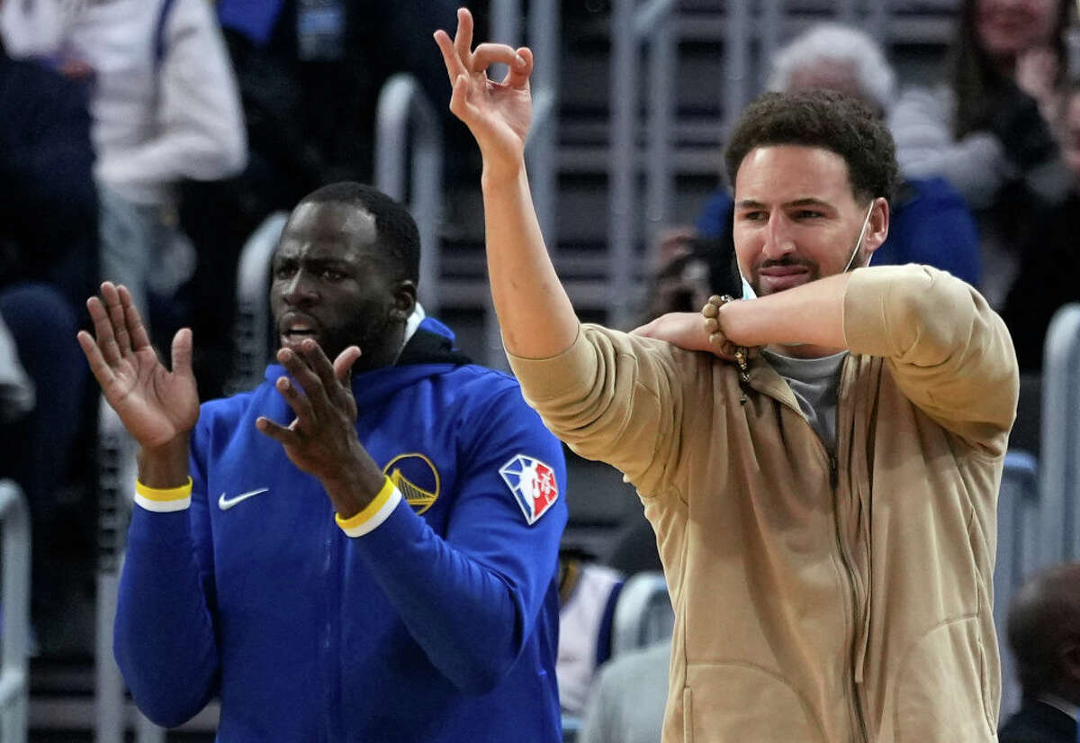 Injured player Klay Thompson, right, and Draymond Green of the Golden State Warriors celebrate on the bench after a teammate make a 3-point shot against the Oklahoma City Thunder during the second quarter at Chase Center on Oct. 30, 2021, in San Francisco. 
