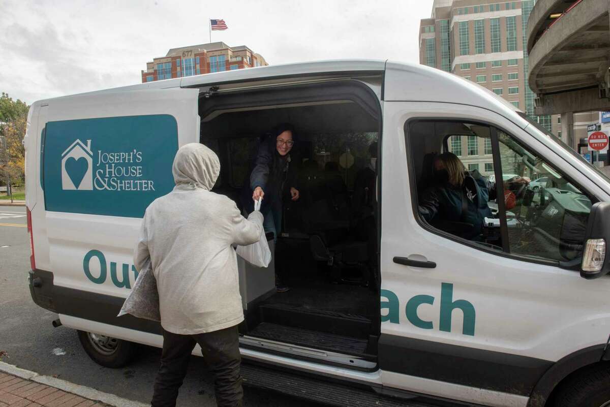 Tiana Minervini, associate director of outreach, left, hands out food and supplies to a homeless person from the new St. Joseph's House outreach van on Wednesday, Oct, 27, 2021 in Albany, N.Y. Shelley Rettinger, director of homeless services, is seen in the driver seat.