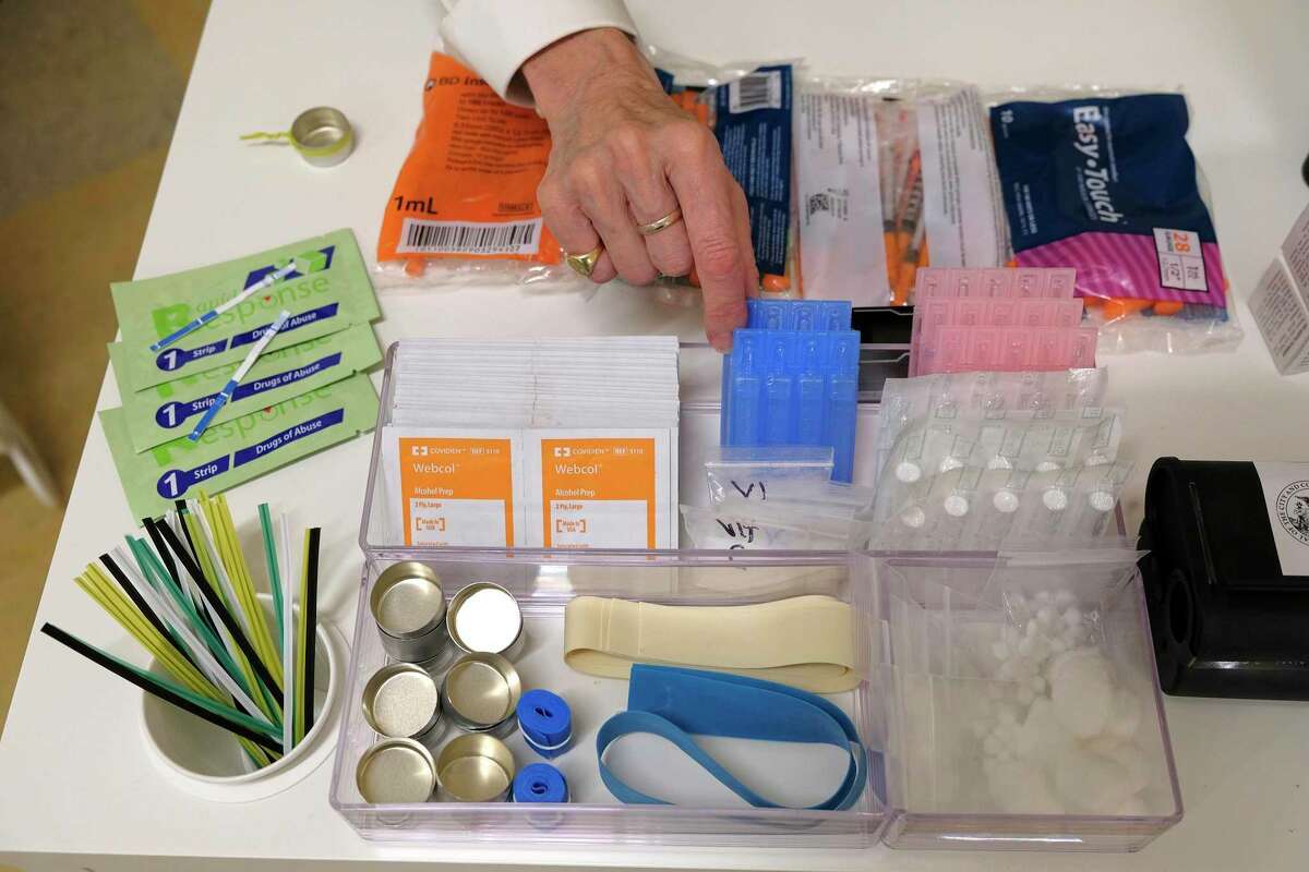 In this photo taken Wednesday, Aug. 29, 2018, Linda Montel shows off supplies on a check in desk at Safer Inside, a realistic model of a safe injection site in San Francisco. The model is an example of a supervised, indoor location where drug users can consume drugs in safer conditions and access treatment and recovery services. (AP Photo/Eric Risberg)