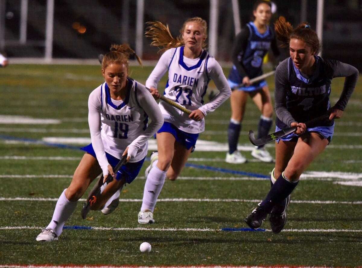 Darien’s Ryan Hapgood (19) moves the ball upfield while defended by Wilton’s Charlotte Casiraghi (4) during the CIAC Class L field hockey semifinals on Tuesday, Nov. 16, 2021 at Norwalk High School’s Sam Testa Field.