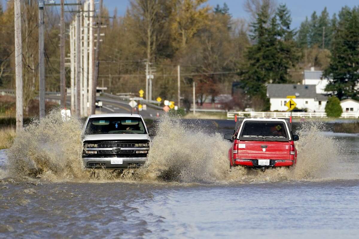 Pickup trucks send up plumes of muddy water as they pass on a flooded road, Tuesday, Nov. 16, 2021, near Everson, Wash. An atmospheric river, a huge plume of moisture extending over the Pacific and into Washington and Oregon, caused heavy rainfall in recent days, bringing major flooding in the area. (AP Photo/Elaine Thompson)