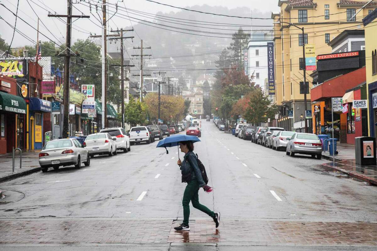 A person crosses Durant Avenue along Telegraph Avenue while carrying an umbrella in Berkeley, Calif. A weak weather system could bring a scant amount of rain to the Bay Area.