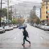 A person crosses Durant Avenue along Telegraph Avenue while carrying an umbrella in Berkeley, Calif. A weak weather system could bring a scant amount of rain to the Bay Area.