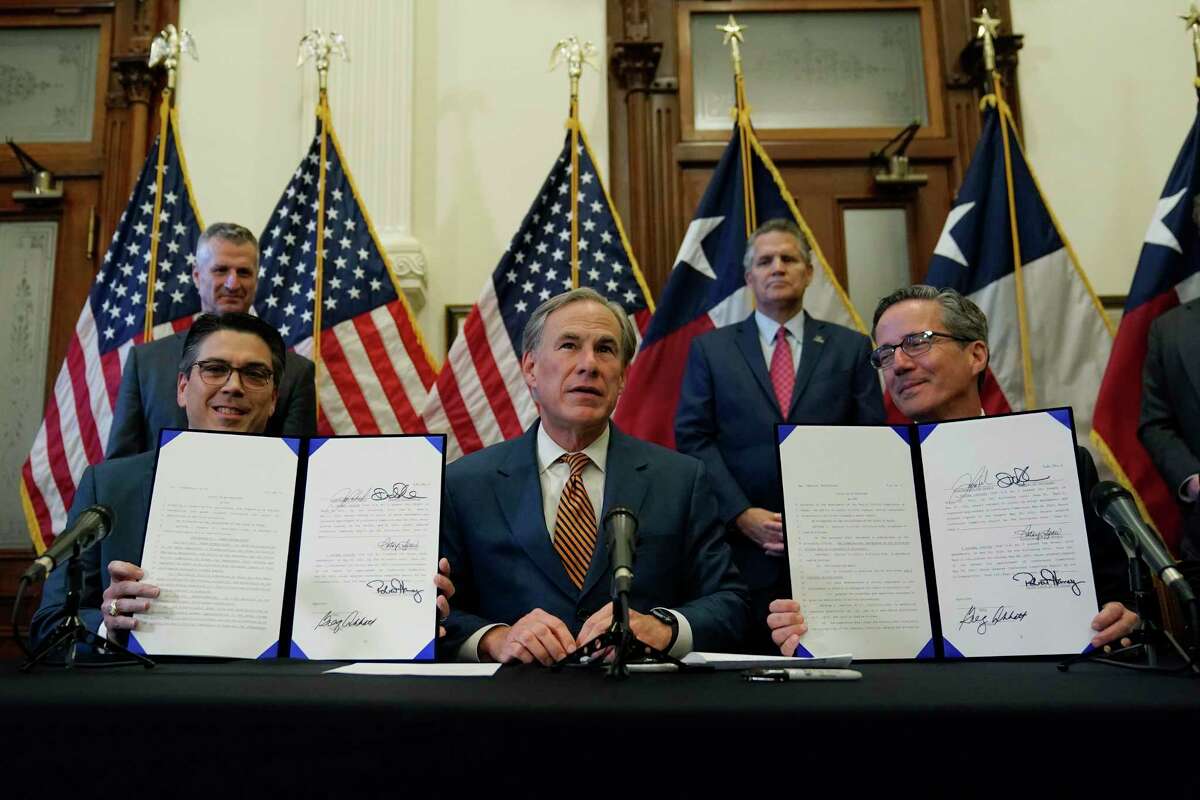 With the help of state Rep. Chris Paddie, left, and state Sen. Kelly Hancock, right, Texas Gov. Greg Abbott, center, speaks as two energy related bills he signed are displayed, Tuesday, June 8, 2021, in Austin, Texas. Abbot signed legislation into law to reform the Electric Reliability Council of Texas (ERCOT) and weatherize and improve the reliability of the state's power grid.